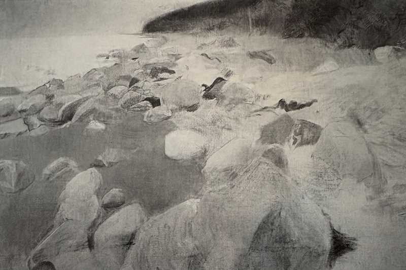 En hvit og steinete strand går i en slak bue innover i bildet. I bakgrunnen ser vi mørkt fjell som stiger opp fra stranden. 