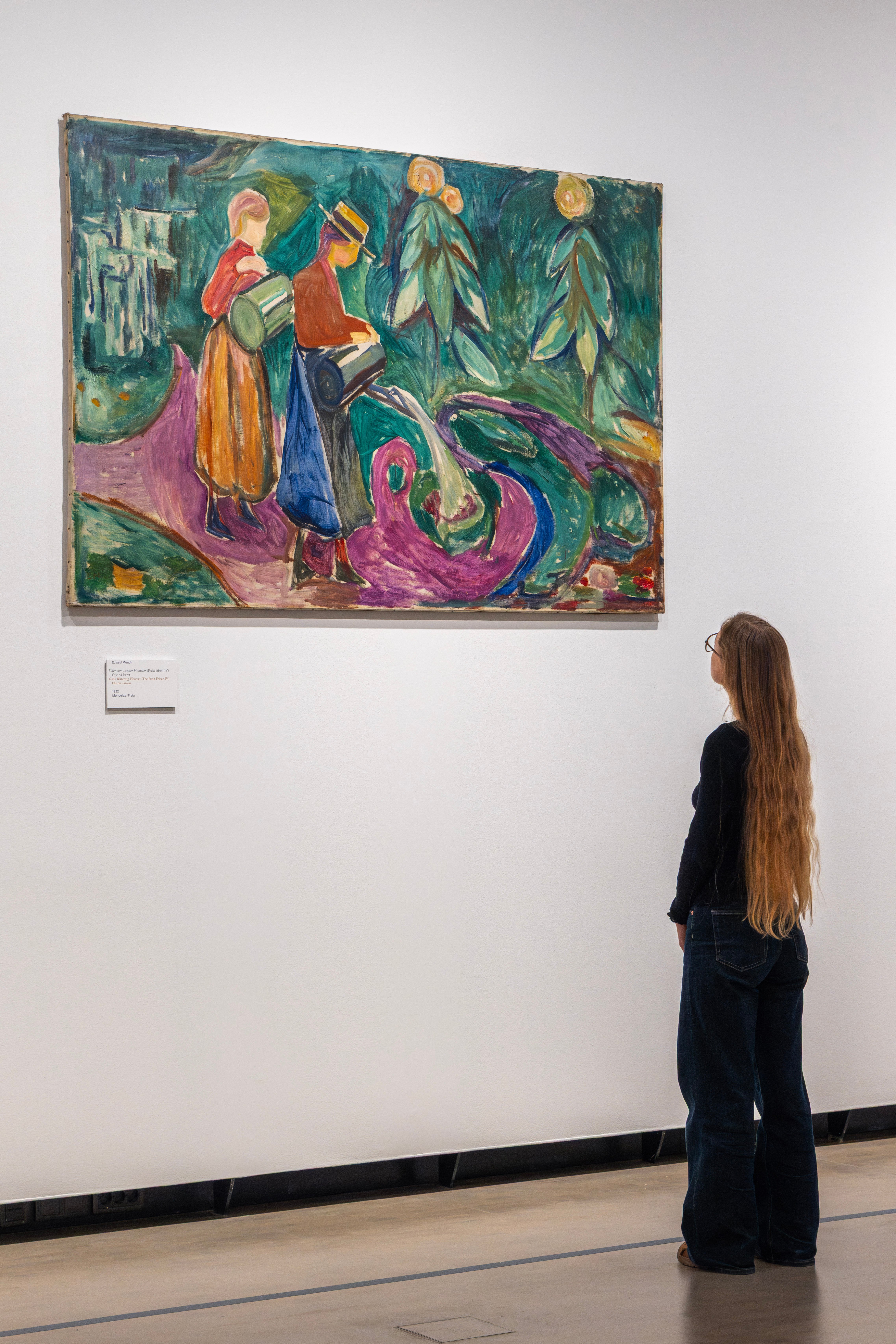 En kvinne med langt hår betrakter verket "Piker vanner blomster" av Edvard Munch. 