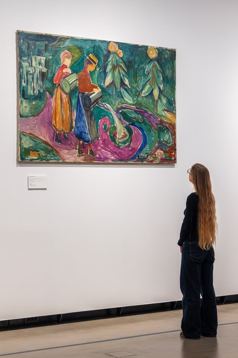 A woman with long hair looks at the work Girls Watering Flowers by Edvard Munch. Photograph.