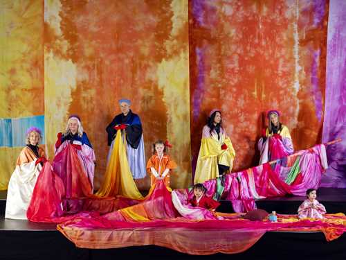 Foto av barn og voksne omringet av fargerike tekstiler.