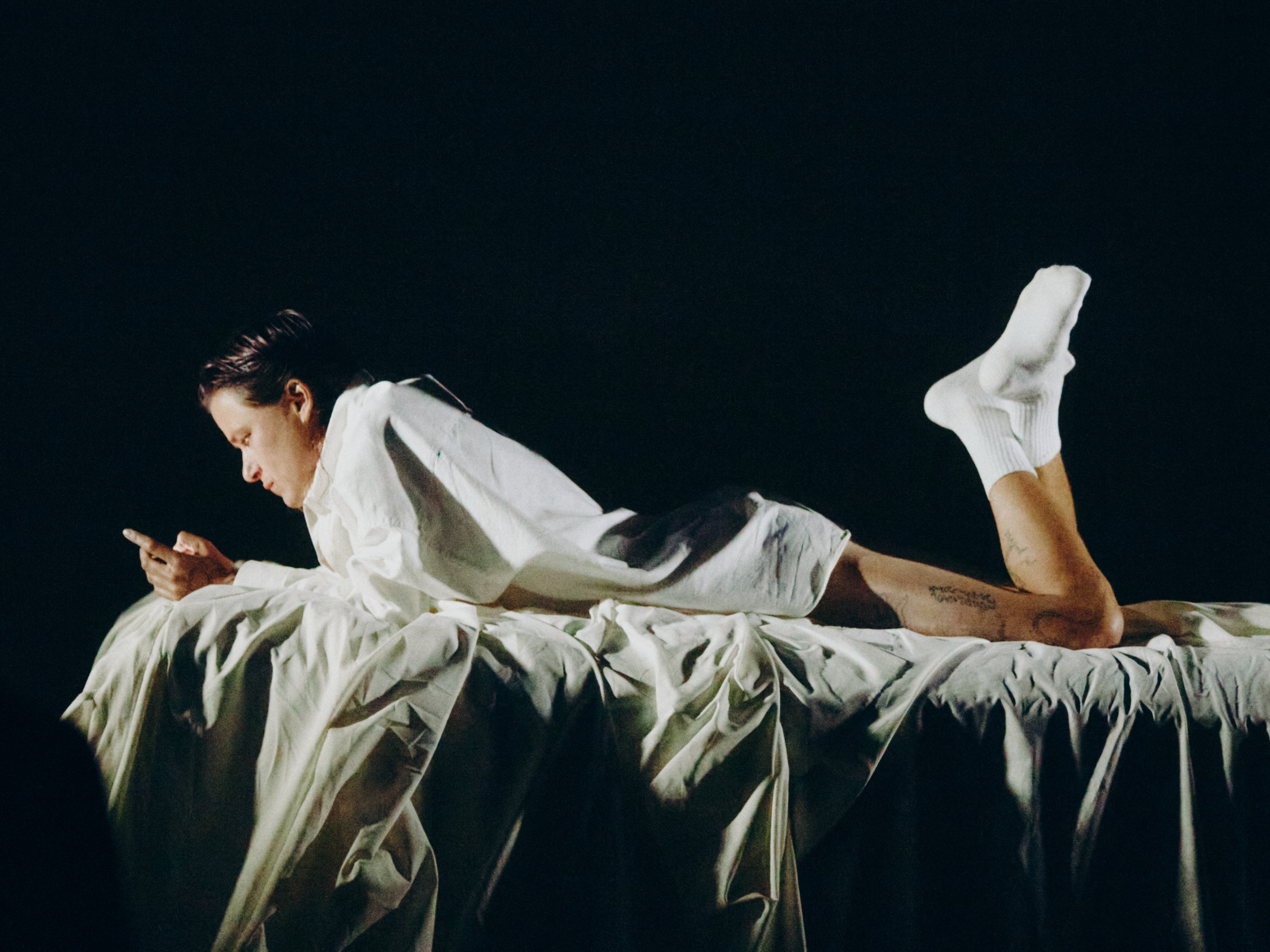 Foto av person som ligger på magen og ser på en mobiltelefon, med sort bakgrunn.