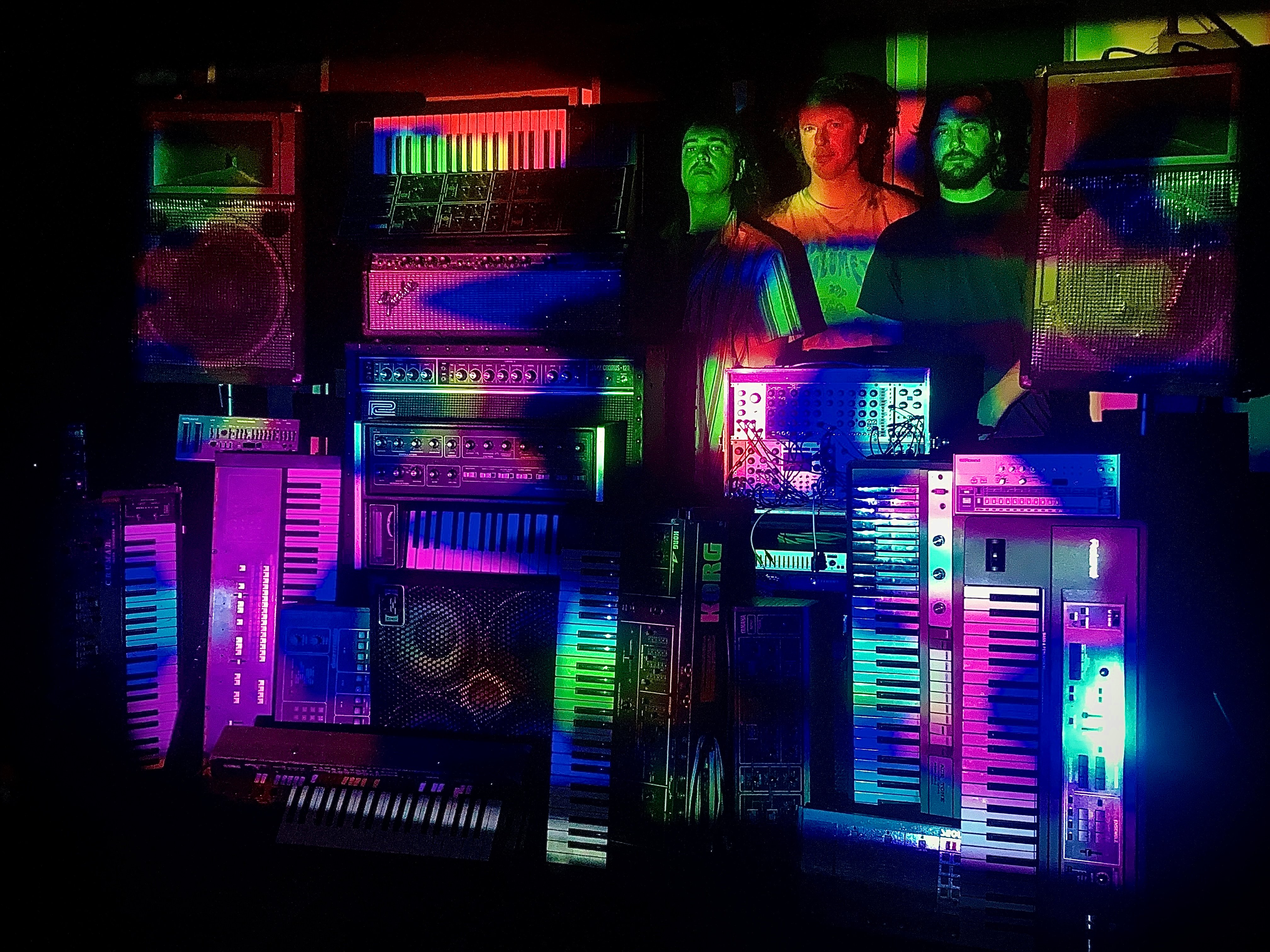 Bilde av en stabel med synthesizere og tre menn som står bak
