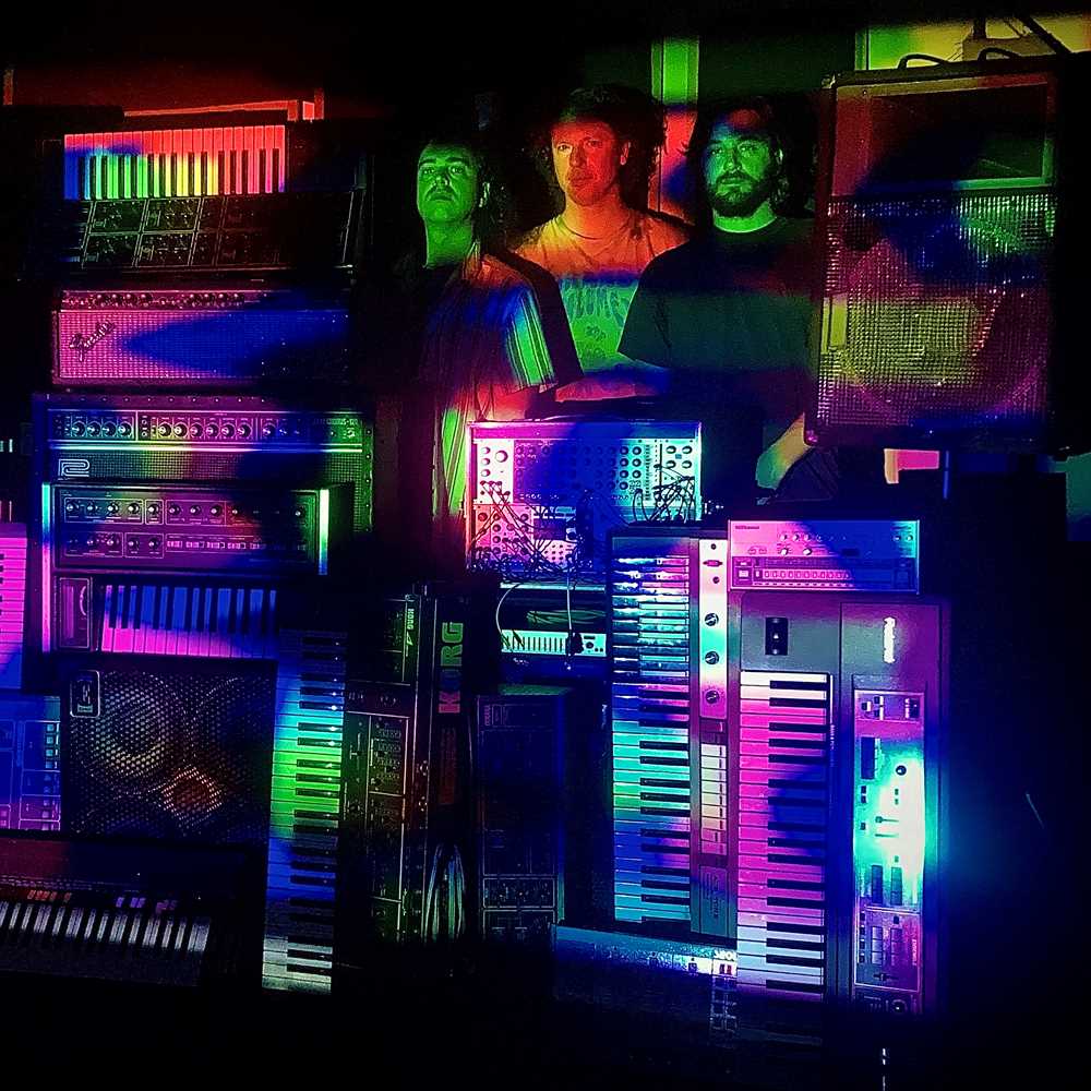 Bilde av en stabel med synthesizere og tre menn som står bak