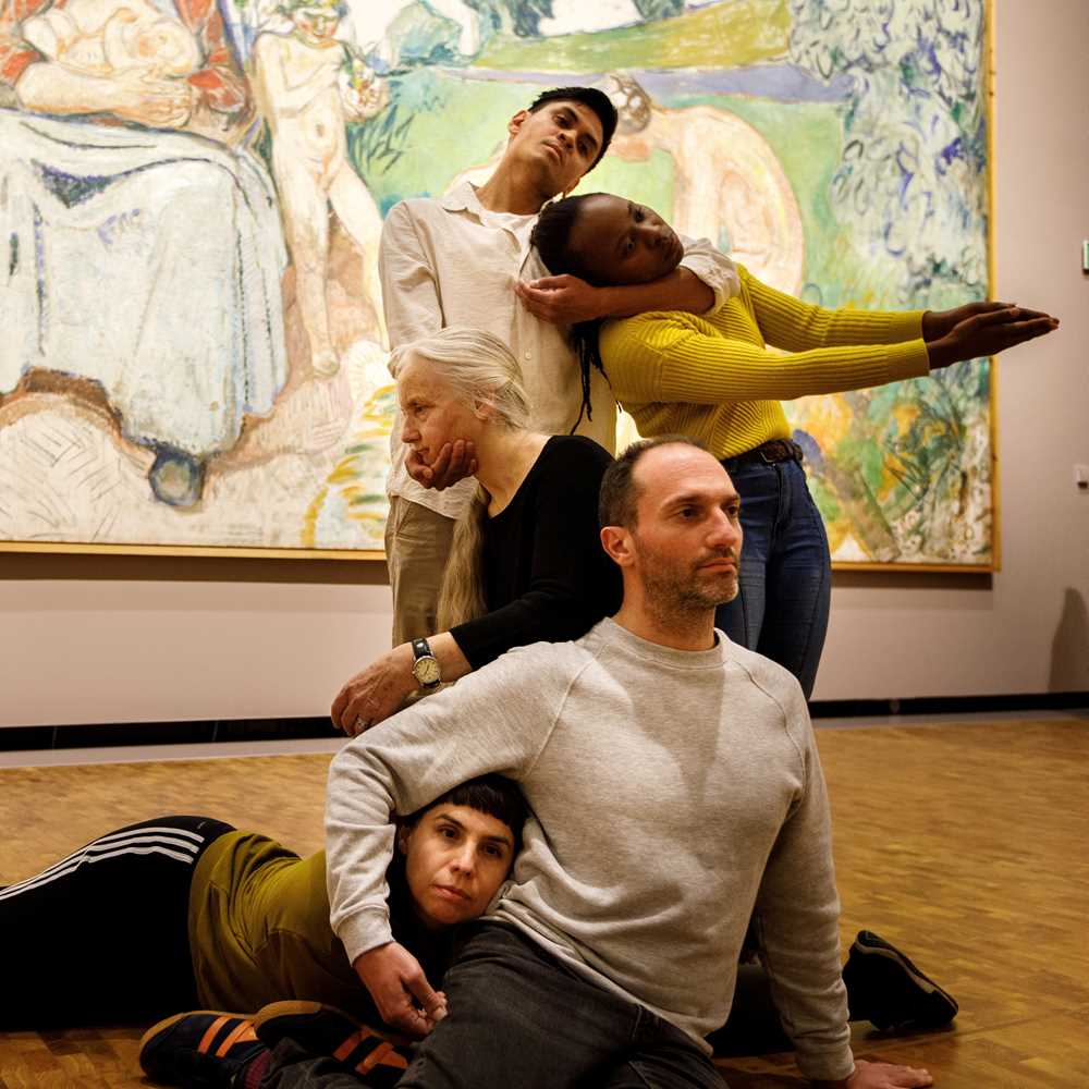 Five dancers in front of Edvard Munch's painting Alma Mater, performing Permanent Collection. They stand, sit, and lie intertwined with one another. Photograph.