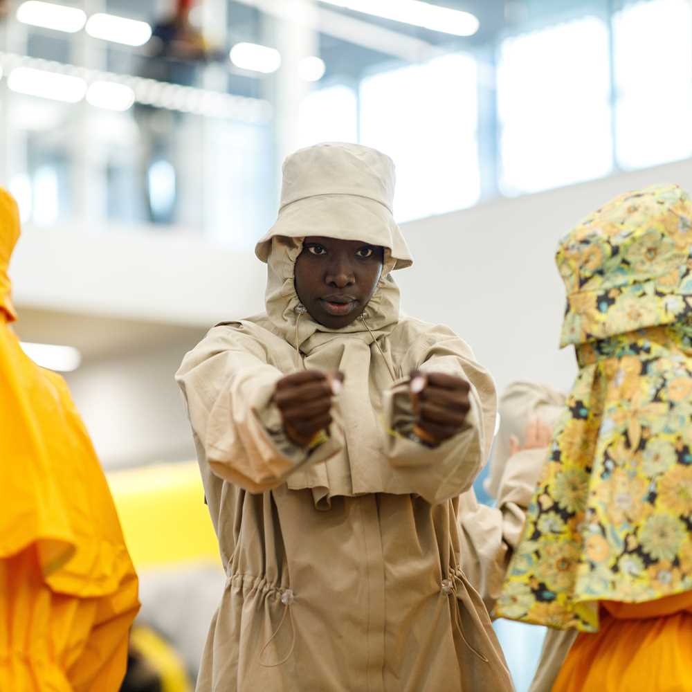 Four people in full rain gear and bucket hats perform a dance in the lobby at MUNCH.